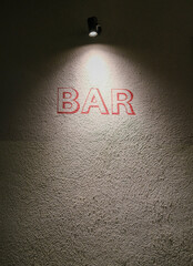 Spotlit wall with the word “BAR” painted in red under a single overhead lamp.