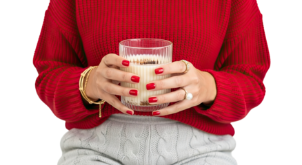 Stylish woman with a festive red manicure wearing a cozy red sweater and gold jewelry holds a glass of a warm, creamy winter drink against an isolated black background