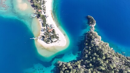 A drone view of the Ölüdeniz peninsula and its turquoise lagoon on the Mediterranean coast of Turkey, surrounded by forested mountains and clear blue water.