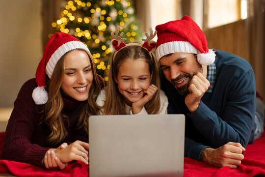 Online Christmas party. Happy family using laptop, making video call while celebrating Xmas distantly, lying on floor at home