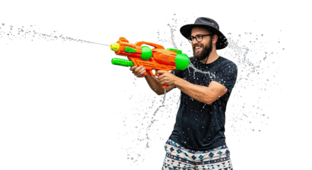 Cheerful young man with a beard wearing a hat and glasses playfully shoots a stream of water from a large toy squirt gun, isolated on a black background