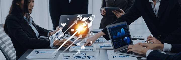 A group of business professionals engages in a strategy session, using technology and data analysis tools to enhance collaboration and foster innovation in a modern office setting. Trope