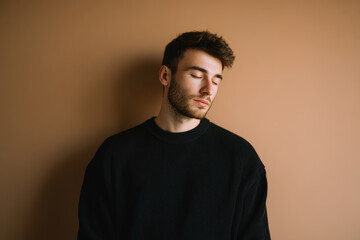 Fototapeta premium young man stands against solid color wall eyes closed exhaling slowly