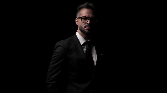 Serious mysterious man in a suit is looking away, then fixing his jacket, and finally crossing his arms on dark background.