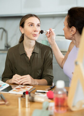 In relaxed home environment, experienced confident female makeup artist delicately brushing blush...