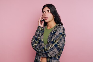 portrait of young woman thoughtfully engages in a phone conversation, illustrating contemplation while standing on pink background