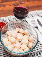 Fine portion of traditional Russian dumplings in a glass bowl, red souse in small glass bowl and glass of fresh red house wine. Fine dinner with simple food.