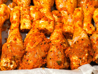 Red hot marinated chicken drumsticks on cooking paper on a old metal cooking tray. Fine poultry product for a large family. Oven cooking.