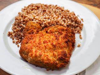 Simple buckwheat meal with breaded chicken fillet on white plate on wooden table. Tasty and healthy food.