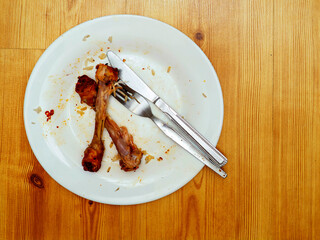 Dirty plate after meal with chicken drumstick bones and fork and knife. Finished dinner with meat.