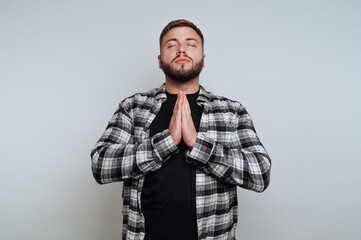 portrait of young contemplative man is seen in a prayer position with closed eyes on white background