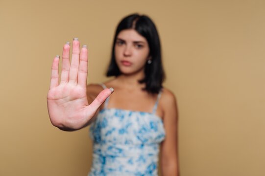 portrait of young woman confidently extends her hand in a stop gesture on beige background