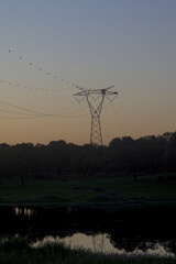 Electricity Pylon Against Darkening Sunset Sky Over Water © MiguelA