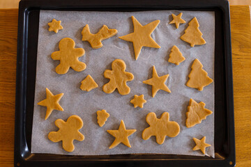 Making gingerbread christmas cookies. Raw gingerbread cookies in tree, star and gingerbread man shapes on baking tray, top view. Winter holiday preparation