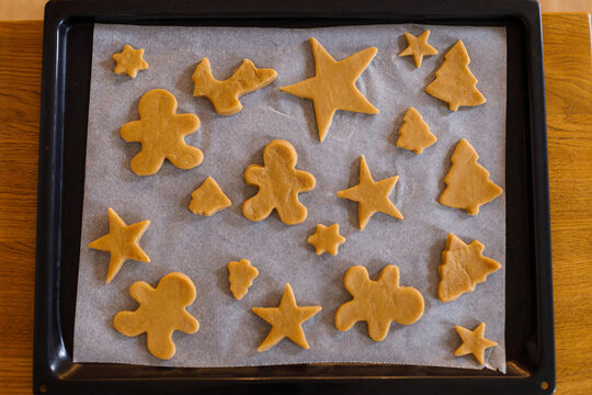 Making gingerbread christmas cookies. Raw gingerbread cookies in tree, star and gingerbread man shapes on baking tray, top view. Winter holiday preparation