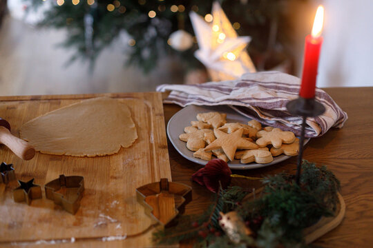 Making gingerbread christmas cookies. Gingerbread cookies on plate, dough, rolling pin and metal cutters on table on background of christmas tree. Winter holiday preparation - Powered by Adobe