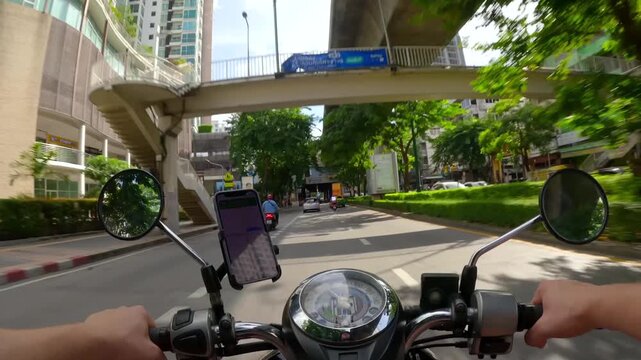 POV shot of scooter ride through Bangkok, Thailand. Rider drives through modern Asian city streets under BTS Skytrain elevated metro line. Urban lifestyle, commuting, and travel adventure.