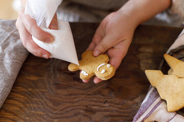 Woman decorating christmas gingerbread cookies with sugar glaze on rustic table top view. Holiday Family tradition