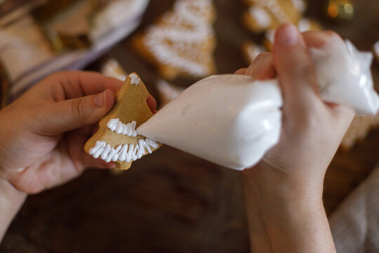 Woman making gingerbread christmas cookies. Hands decorating cookies with icing on table close up. Winter holiday preparation - Powered by Adobe