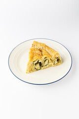 Slice of savory filo pie with cheese and herbs on plate, isolated on white