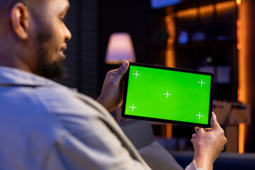 Young male freelancer uses green screen mockup on modern tablet to work in the living room, sitting...