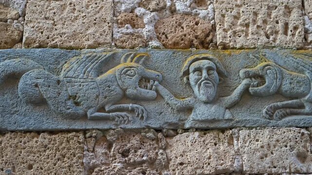 Medieval stone bas-relief of a man taming two mythical beasts. Detailed close-up of a medieval stone carving on an ancient church wall in viterbo, italy