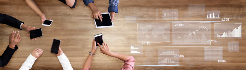 A dynamic overhead view of diverse hands engaged with various digital devices on a wooden table,...