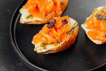 Gourmet salmon canapes on baguette with cream cheese and cucumber on black plate