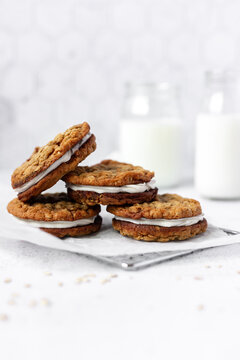 Straight-on view of oatmeal cream pie cookies stacked together with glasses of milk in the background.