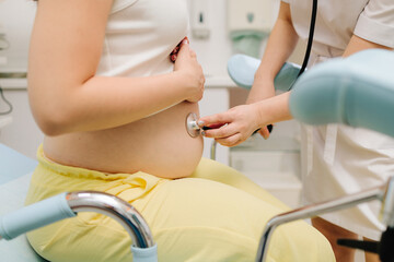 Obraz premium Pregnancy checkup. Gynecologist with stethoscope listening baby heartbeat in patient tummy on appointment in gynecology clinic.