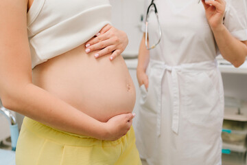 Pregnancy checkup. Gynecologist with stethoscope listening baby heartbeat in patient tummy on...