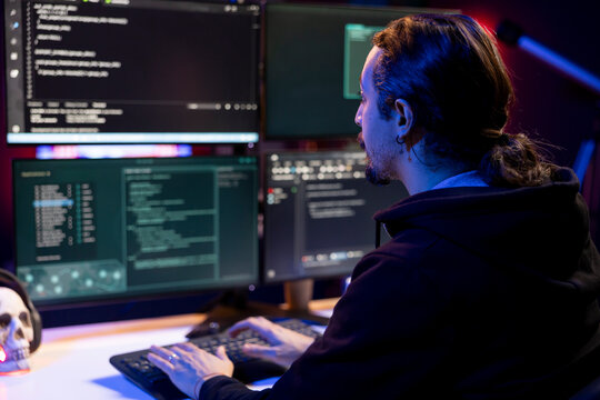 Hacker in neon lit criminal den coding malware designed to exploit network backdoors. Rogue engineer typing on keyboard, bypassing security measures such as logins and password protections - Powered by Adobe