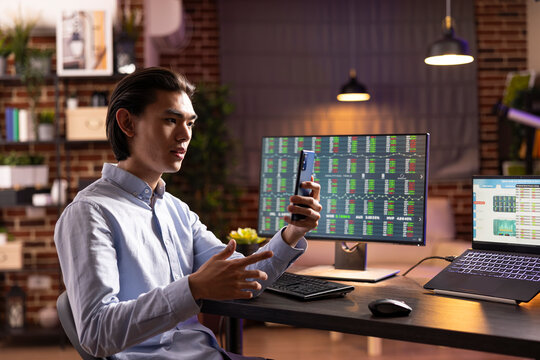 Self employed man speaking with business partner during online meeting. Asian male entrepreneur manages company tasks, sharing marketing strategy plans with colleagues through cellphone video call.