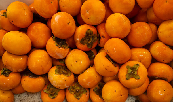 Freshly harvested ripe orange persimmons piled up at a market stall, showing their smooth skin and calyx.