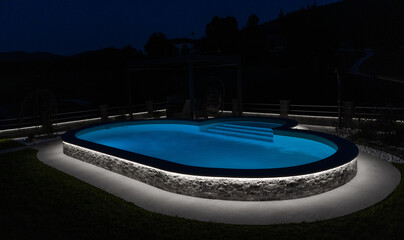 A modern outdoor pool glowing at night with vibrant LED lighting inside and around the water, creating a luxurious, serene, and atmospheric scene ideal for relaxation and nightlife visuals.