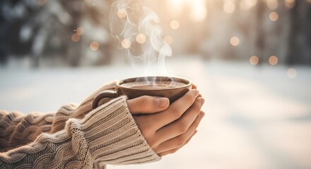 Hands in a cozy knit sweater holding a steaming mug of a hot drink on a cold, snowy winter morning.