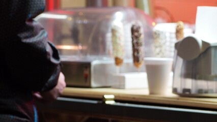 Sweets and drinks at the Christmas market. Stylish christmas illumination and fir branches with red and gold baubles, golden lights bokeh on front of building at holiday market in city street.Christma