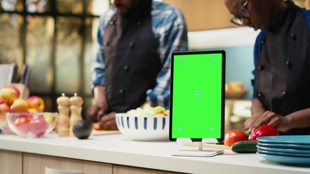 Vertical chroma key tablet with lovers doing meal prep for a salad, preparing food at the kitchen counter. Couple enjoying time together in the kitchen, cooking with aprons and having fun. Camera B.