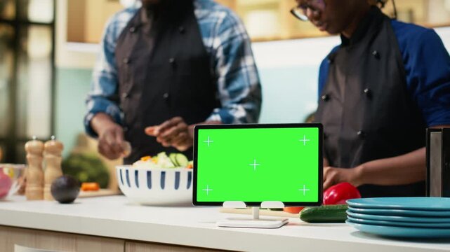Isolated mockup tablet next to people doing meal prep in the kitchen, man and woman cooking and spending time together at home. Happiness and healthy lifestyle, bonding with joy. Camera B.