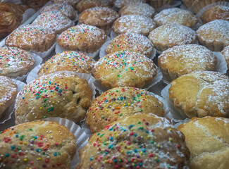 A close-up view of traditional Italian cookies, likely Anginetti (Italian Wedding Cookies) or similar soft Italian cookies, dusted with powdered sugar and decorated with rainbow sprinkles. 