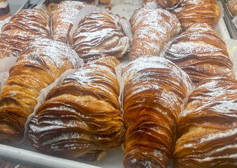 Flaky, golden sfogliatelle pastries stacked in a bakery display, their crisp layered shells dusted with powdered sugar and filled with sweet, creamy ricotta for a classic Italian treat.
