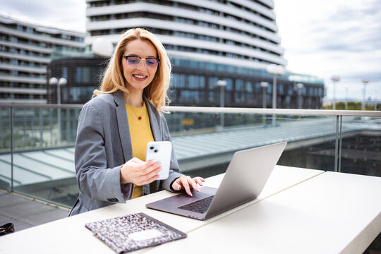Businesswoman working remotely outdoors, using smartphone and laptop