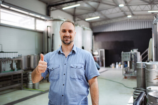 Brewery owner smiling and giving thumbs up in craft beer factory - Powered by Adobe