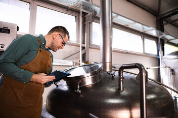 Man wearing apron checking beer fermentation on tablet in microbrewery