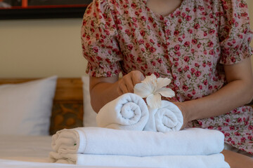 Hands of hotel maid putting plumeria flower and towels on the bed in the luxury hotel room ready for tourist travel