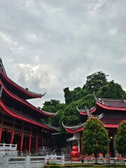 Obraz premium Side area of Sam Poo Kong Temple, Semarang, featuring traditional red buildings, layered curved roofs, and surrounding lush greenery, highlighting the peaceful atmosphere of this historic complex.