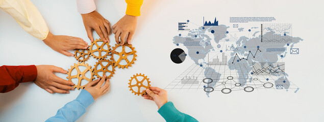 A diverse group of people engages with wooden gears and business charts, symbolizing teamwork and innovation in a modern workspace designed for strategic planning. Trope