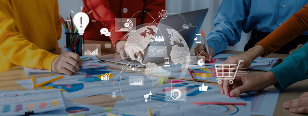 A dynamic group of professionals engaged in a collaborative meeting, analyzing data and strategizing over documents and a laptop in a modern office setting. Trope