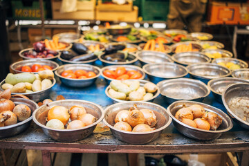 Bowls of onions, tomatoes, potatoes, and eggplants displayed at an outdoor market stall