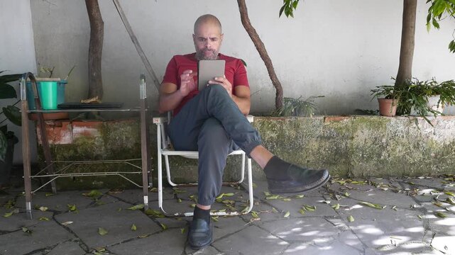 Literature: A person reads an e-reader in the backyard. A man reads an e-book on his e-reader. Someone reading a book. Book Day.